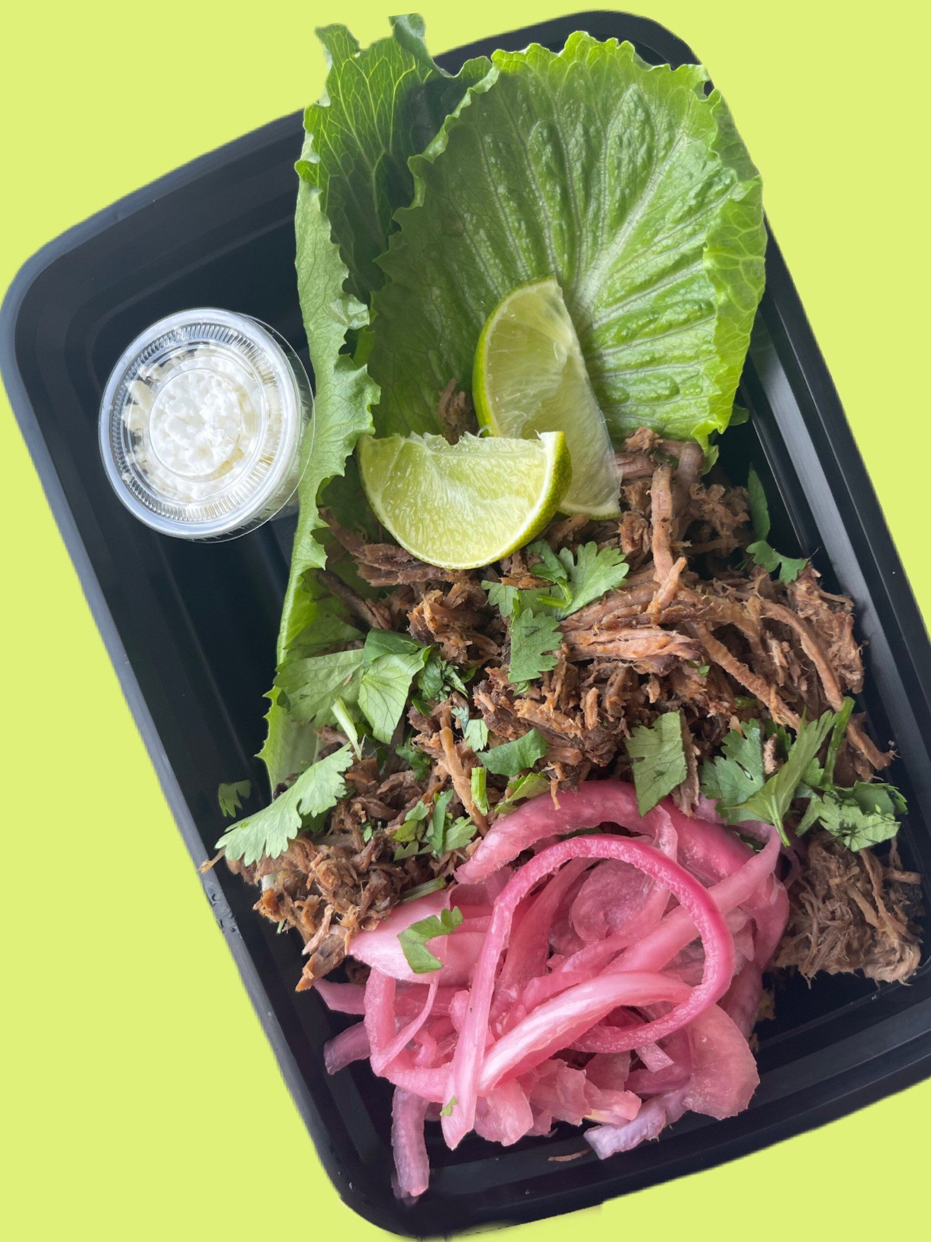 A tray of food with lettuce , onions , limes and sour cream.