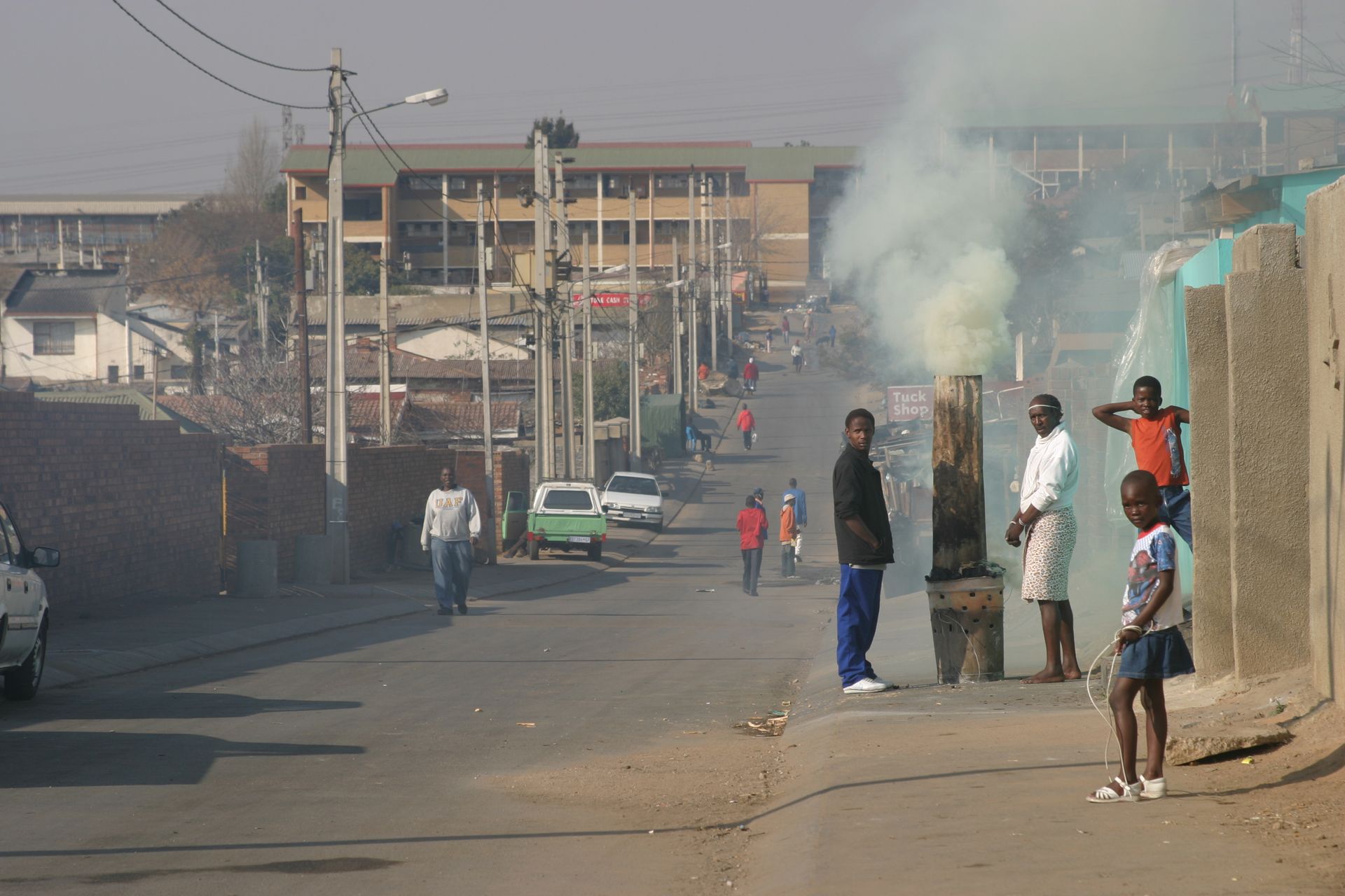 A group of people standing on the side of a street with smoke coming out of a chimney.