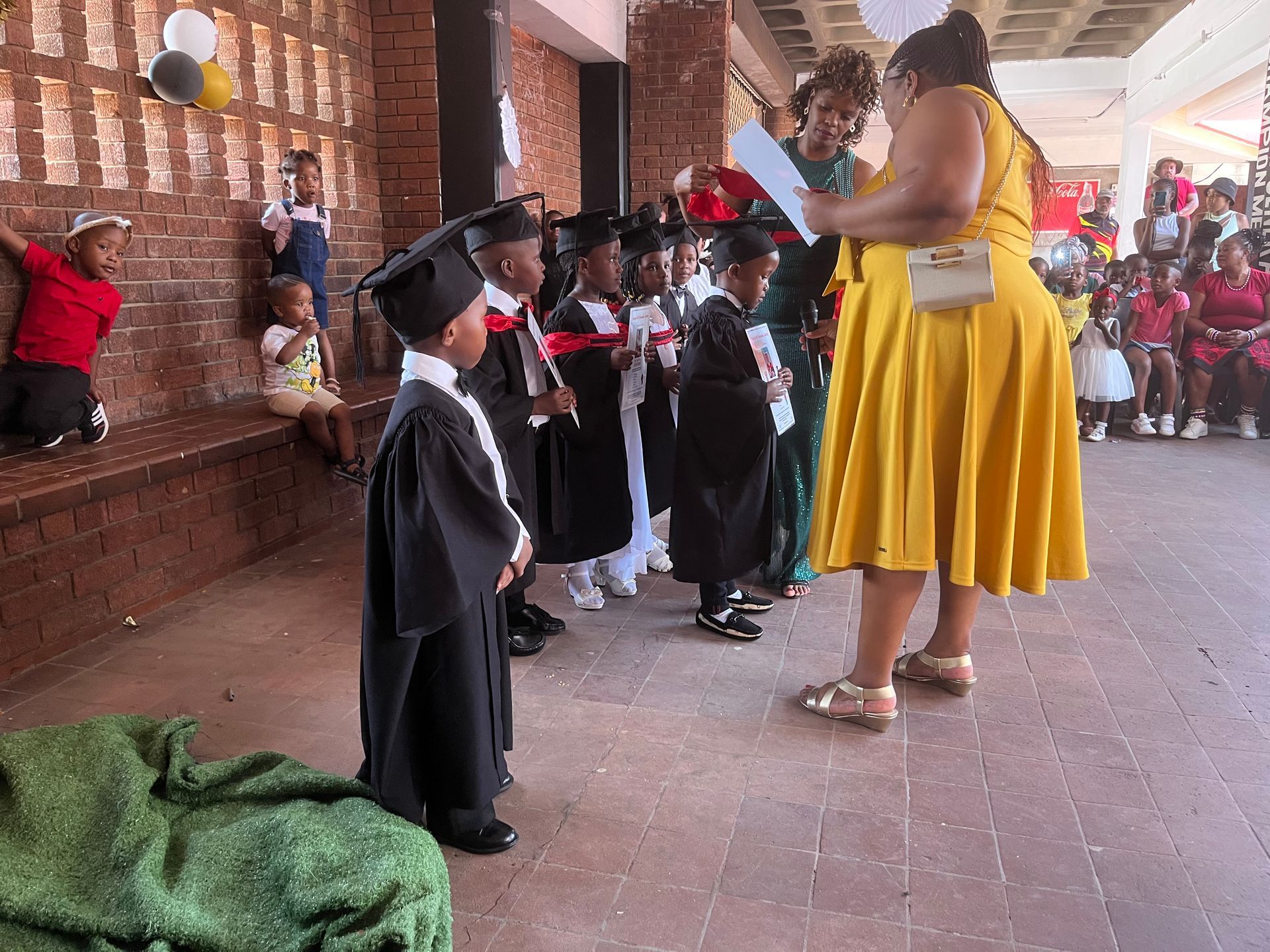A woman in a yellow dress is standing next to a group of children in graduation caps and gowns.