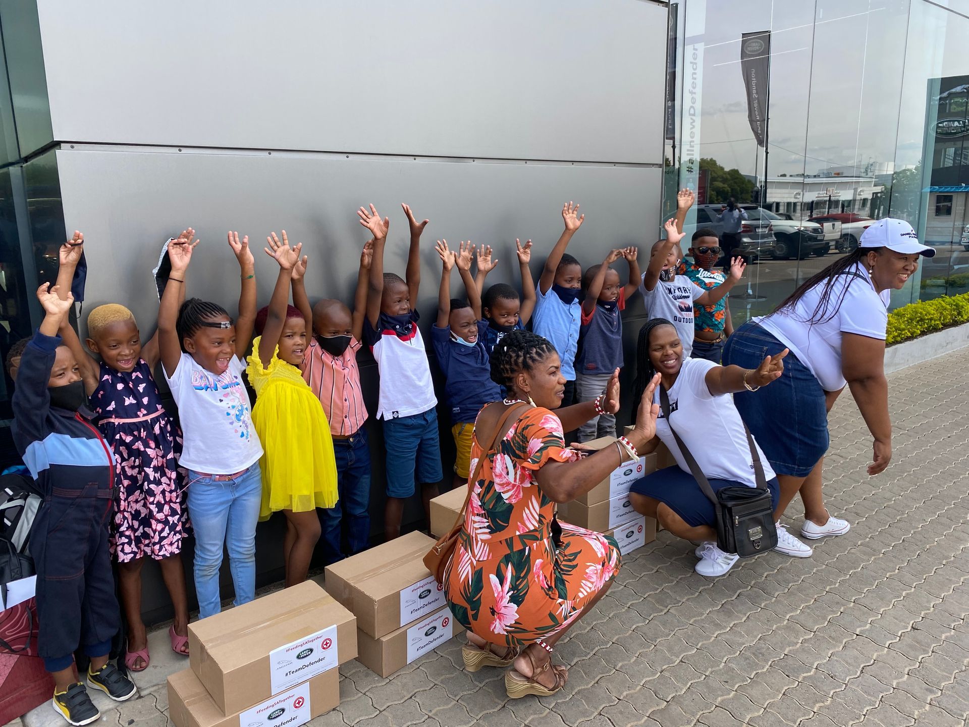 A group of children are standing in front of a building with their hands in the air.