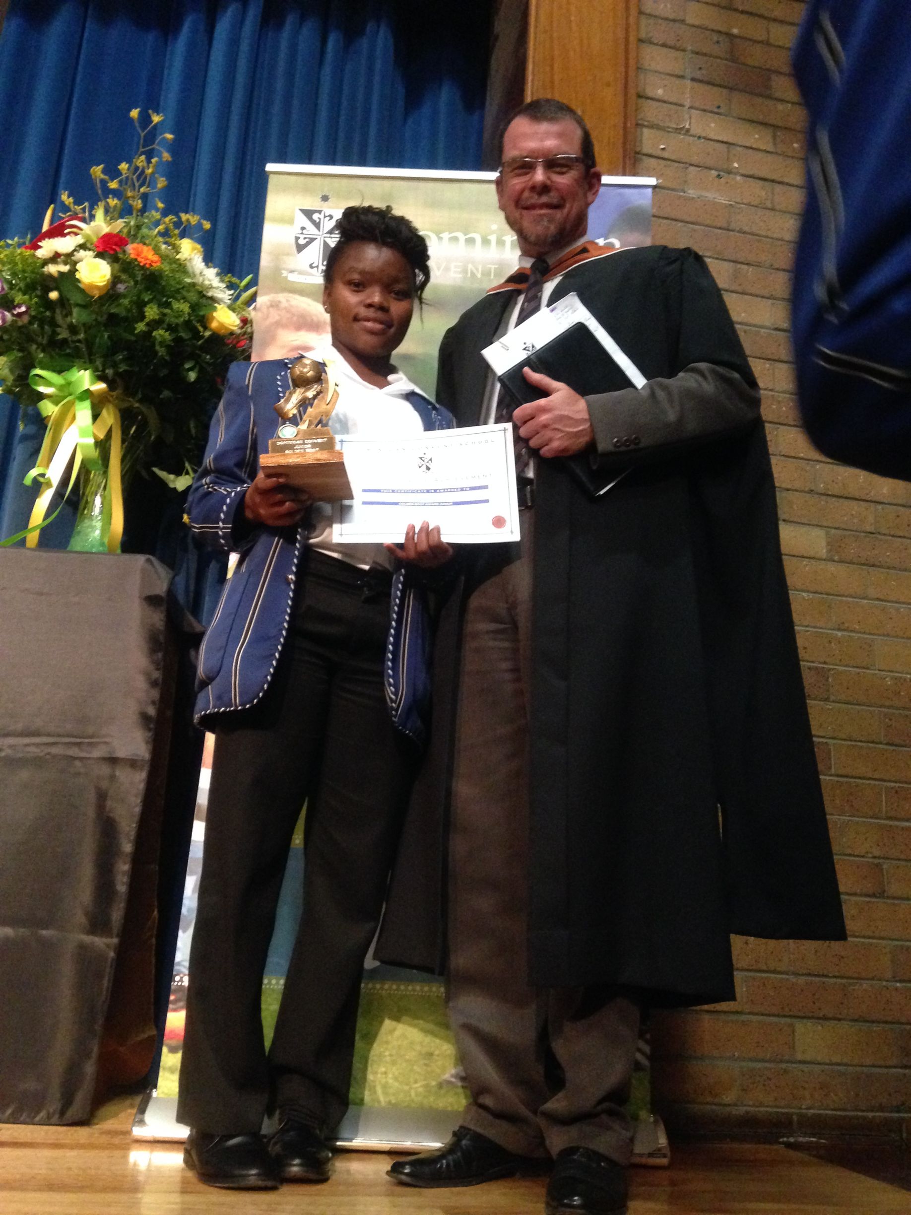 A man and a woman are standing next to each other holding a trophy and a certificate.