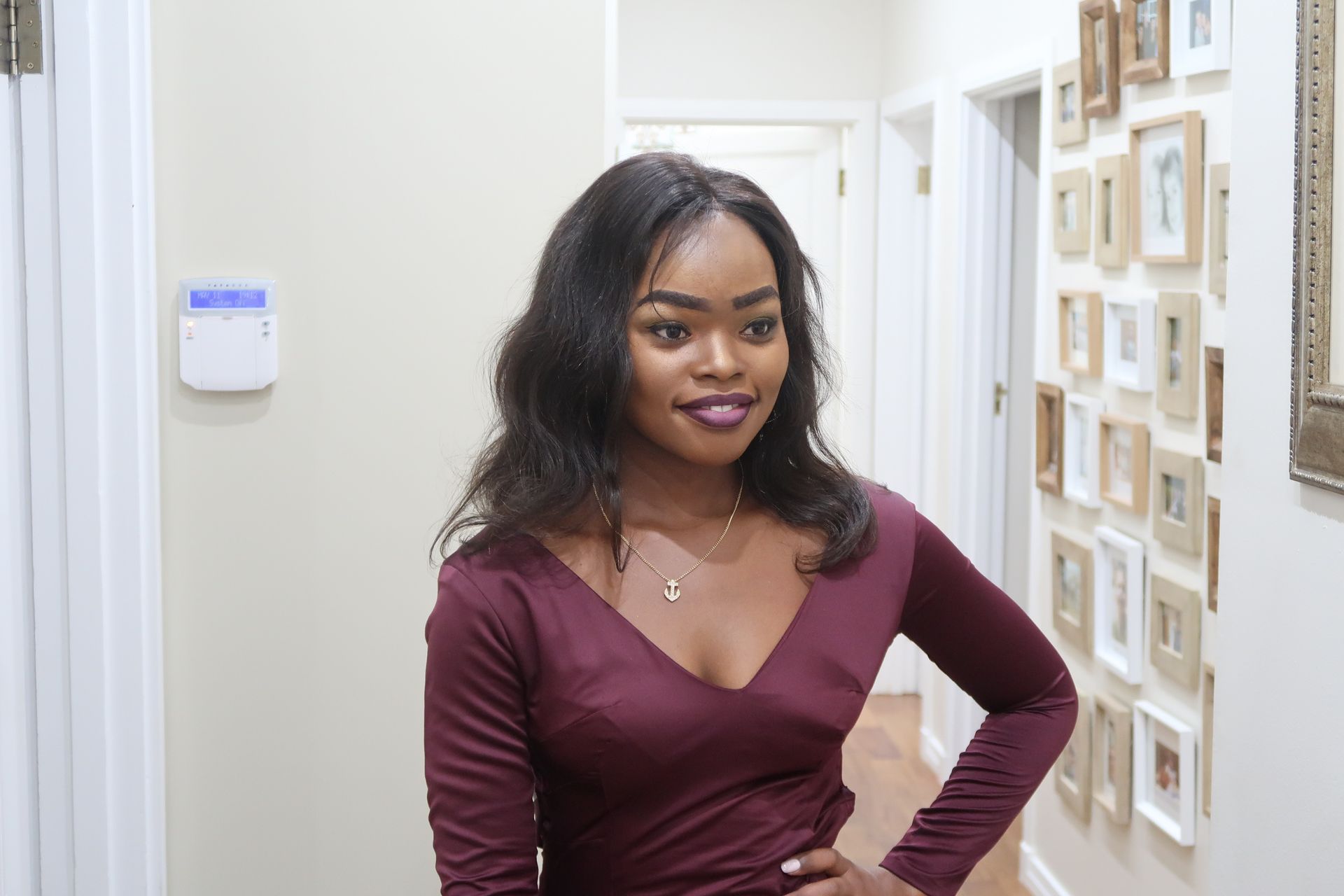 A woman in a burgundy dress is standing in a hallway with her hands on her hips.