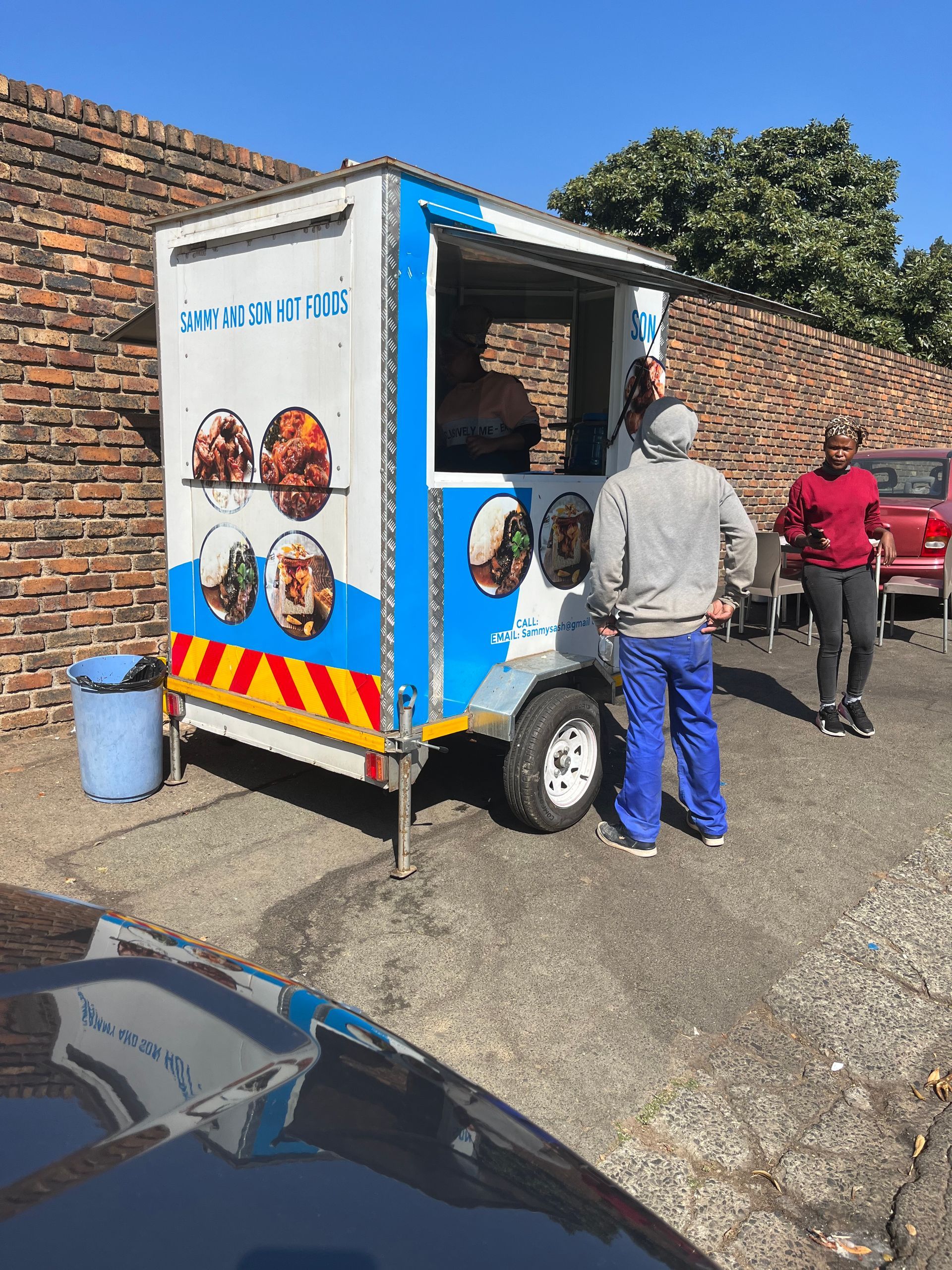 A man is standing in front of a food truck in a parking lot.
