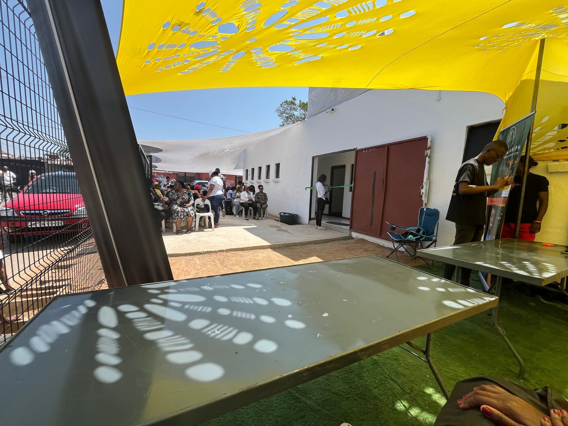 A group of people are standing outside of a building under a yellow umbrella.