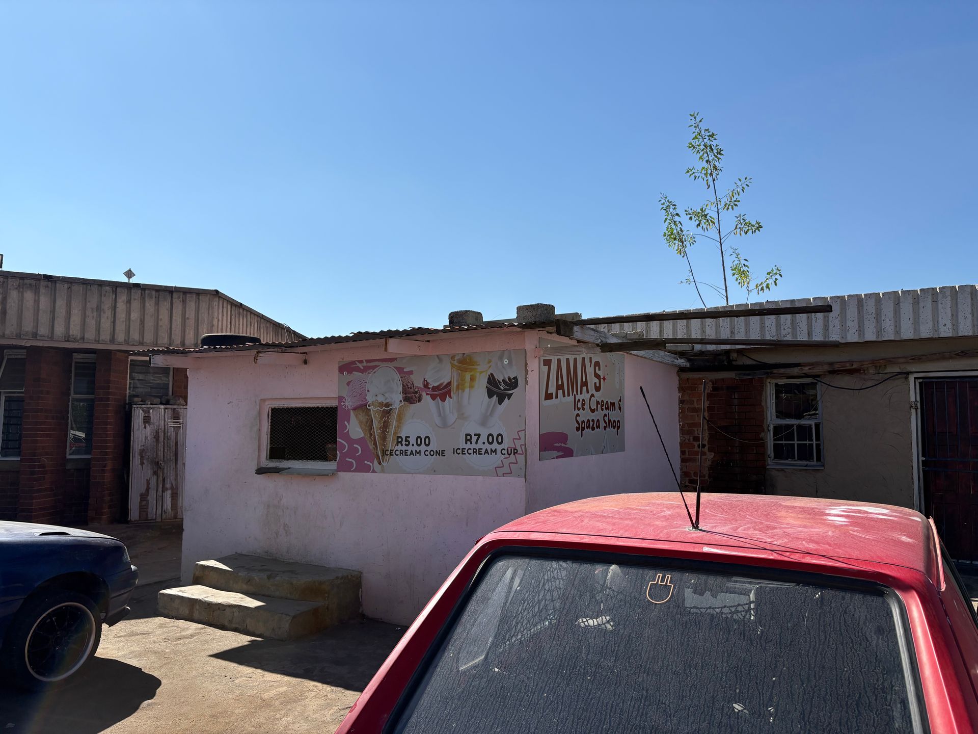 A red car is parked in front of a pink building