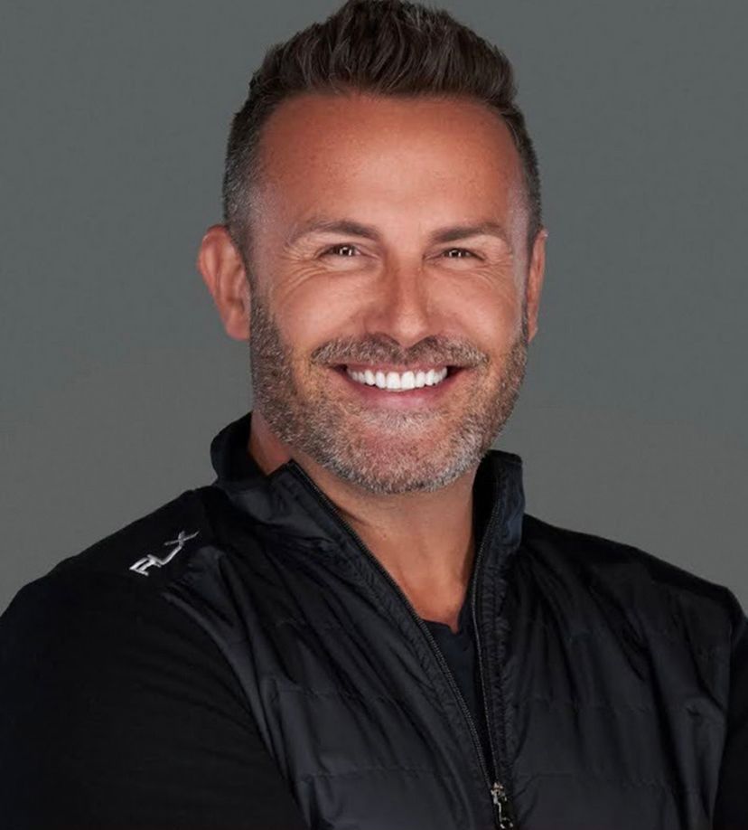 A man with a beard is smiling for the camera while wearing a black jacket.