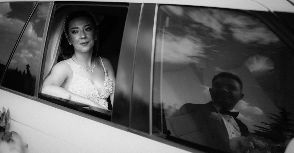 A bride and groom are sitting in a car looking out the window.