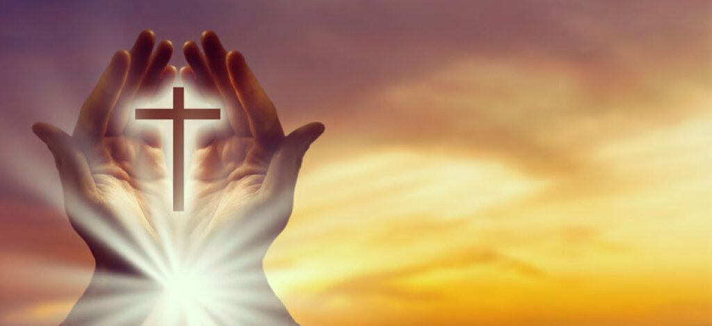 Hands cupping a glowing cross at sunrise with warm golden light