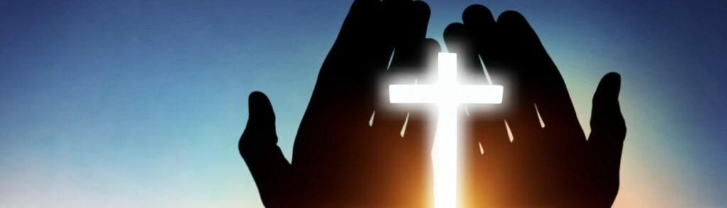 Silhouetted hands raised around a glowing cross at sunset