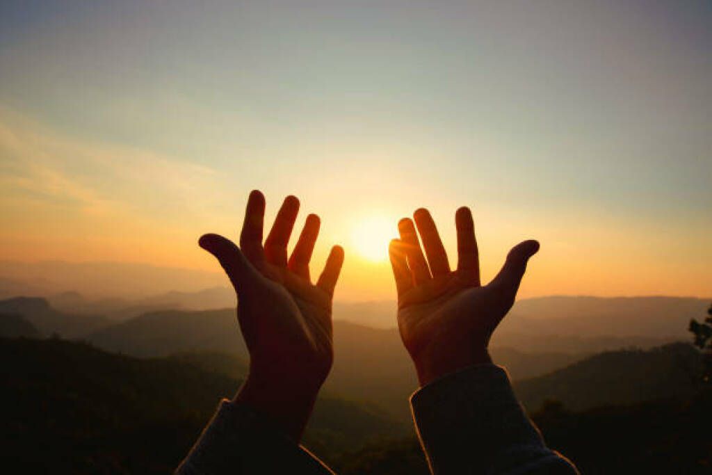 Hands raised toward the setting sun over a mountain landscape