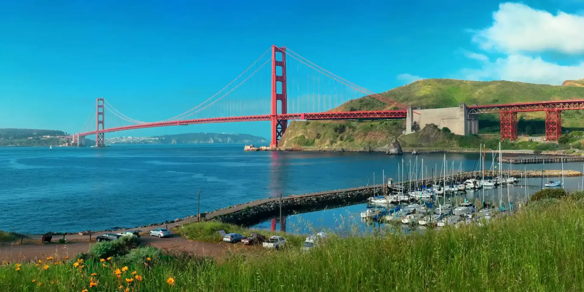 Golden Gate Bridge in San Francisco, California, spanning a bay with boats, hills, and a clear blue sky.
