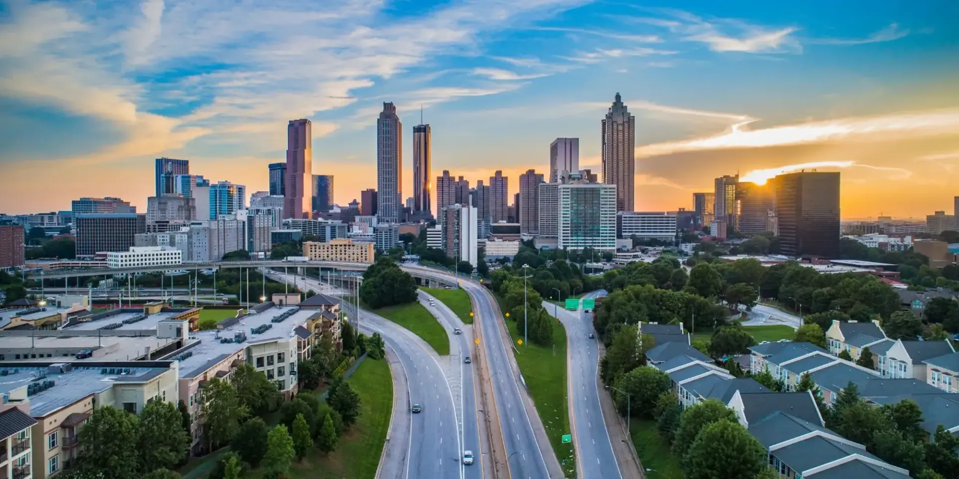 Atlanta skyline at sunset, with highways and residential areas in the foreground, against a blue and orange sky.