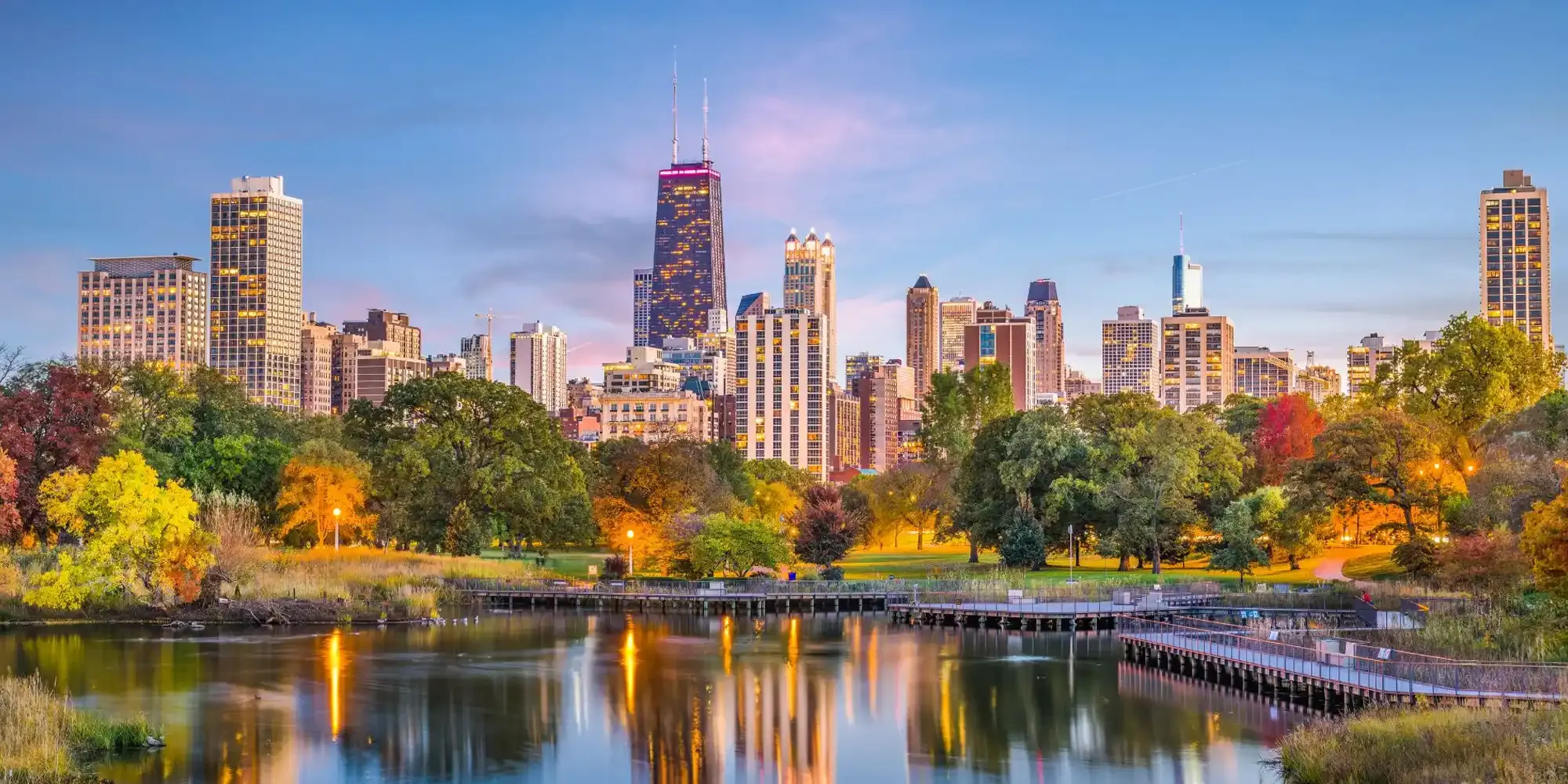 Chicago skyline with buildings and park reflected in water.