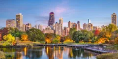 Chicago skyline framed by a park, with reflection in the water and colorful trees.