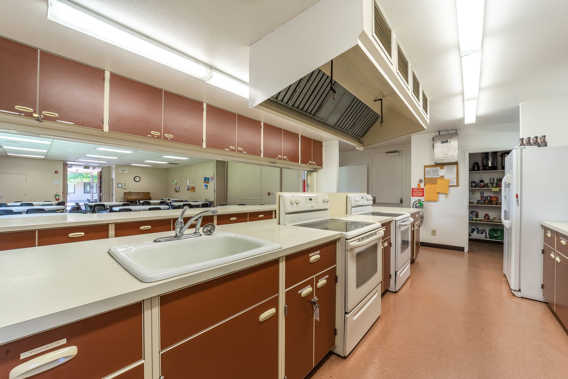A large commercial kitchen with brown cabinets and white appliances
