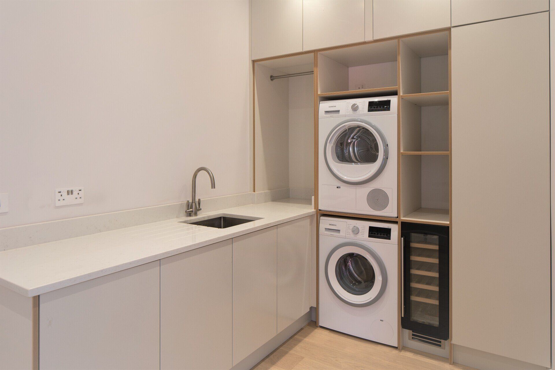 Utility room with porcelain units with plywood edging and washing machine and tumble dryer stacked on top of each other.