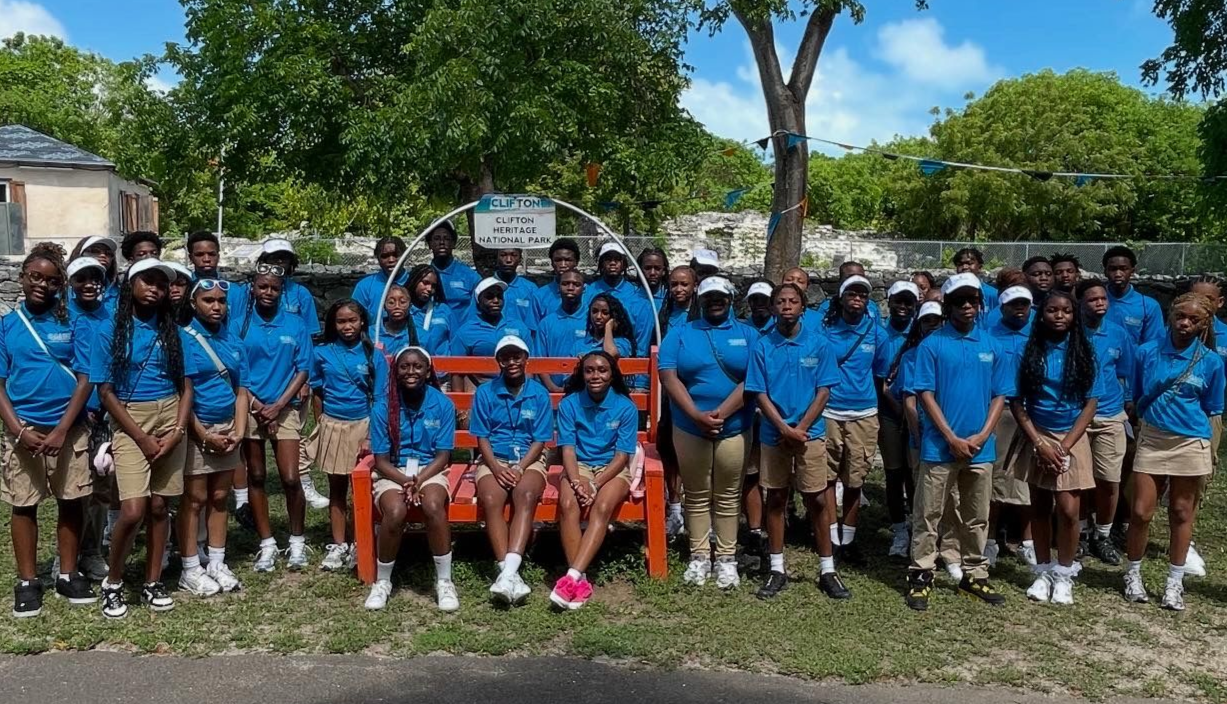 Group of people in blue shirts and khaki shorts standing near an orange bench outdoors.