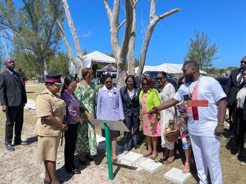 Group of people around a plaque at a tree planting ceremony outdoors.