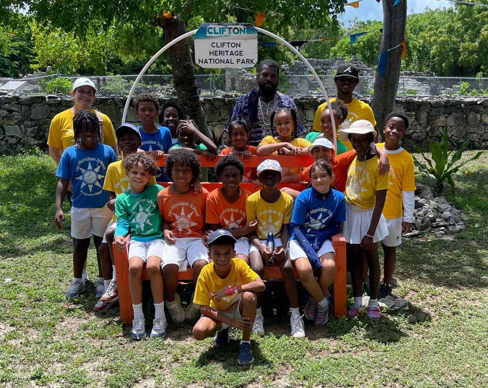Group of children in colorful shirts pose on a wooden bench outdoors.