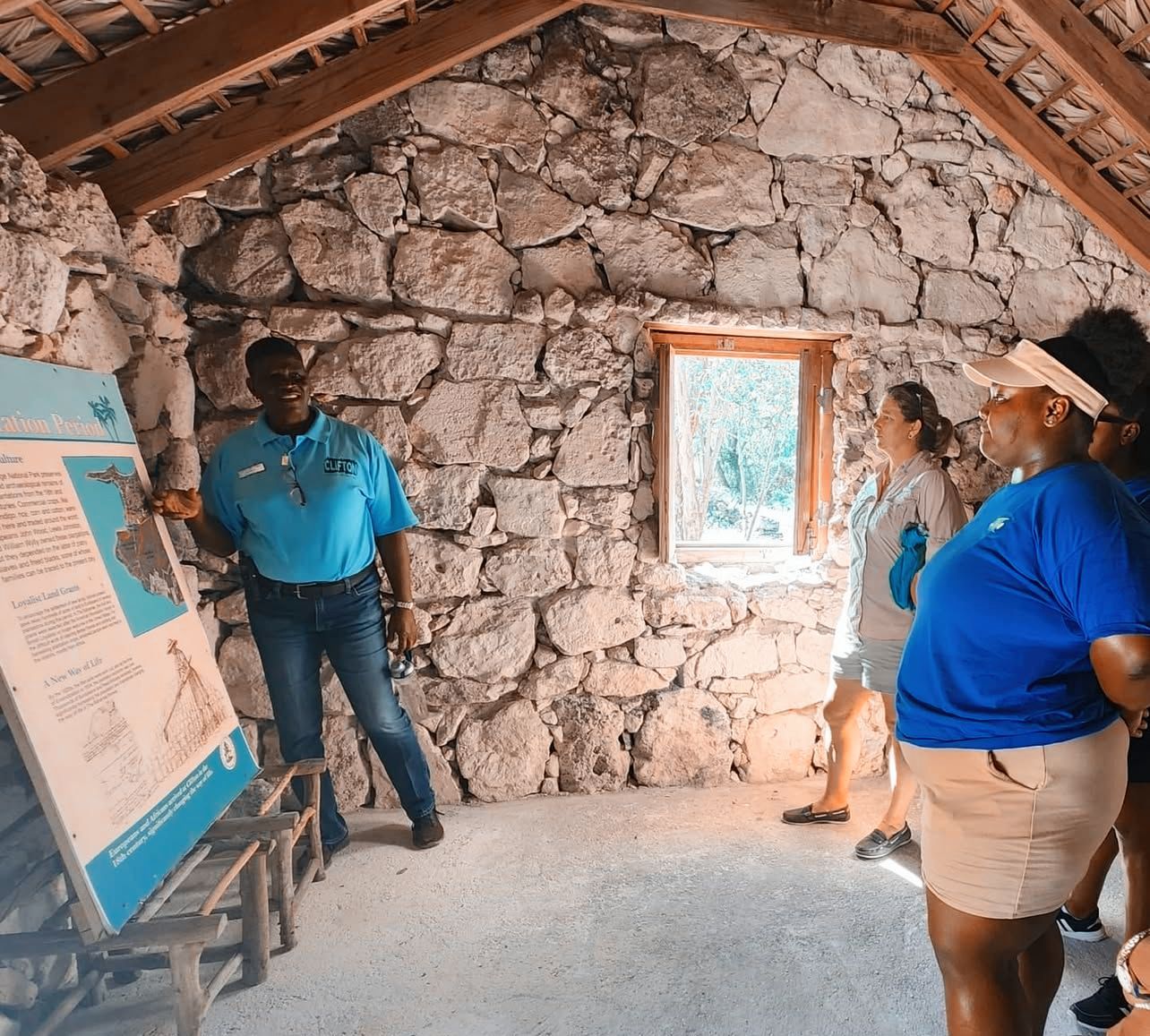 Tour guide points at map, explaining to a small group inside a stone building.