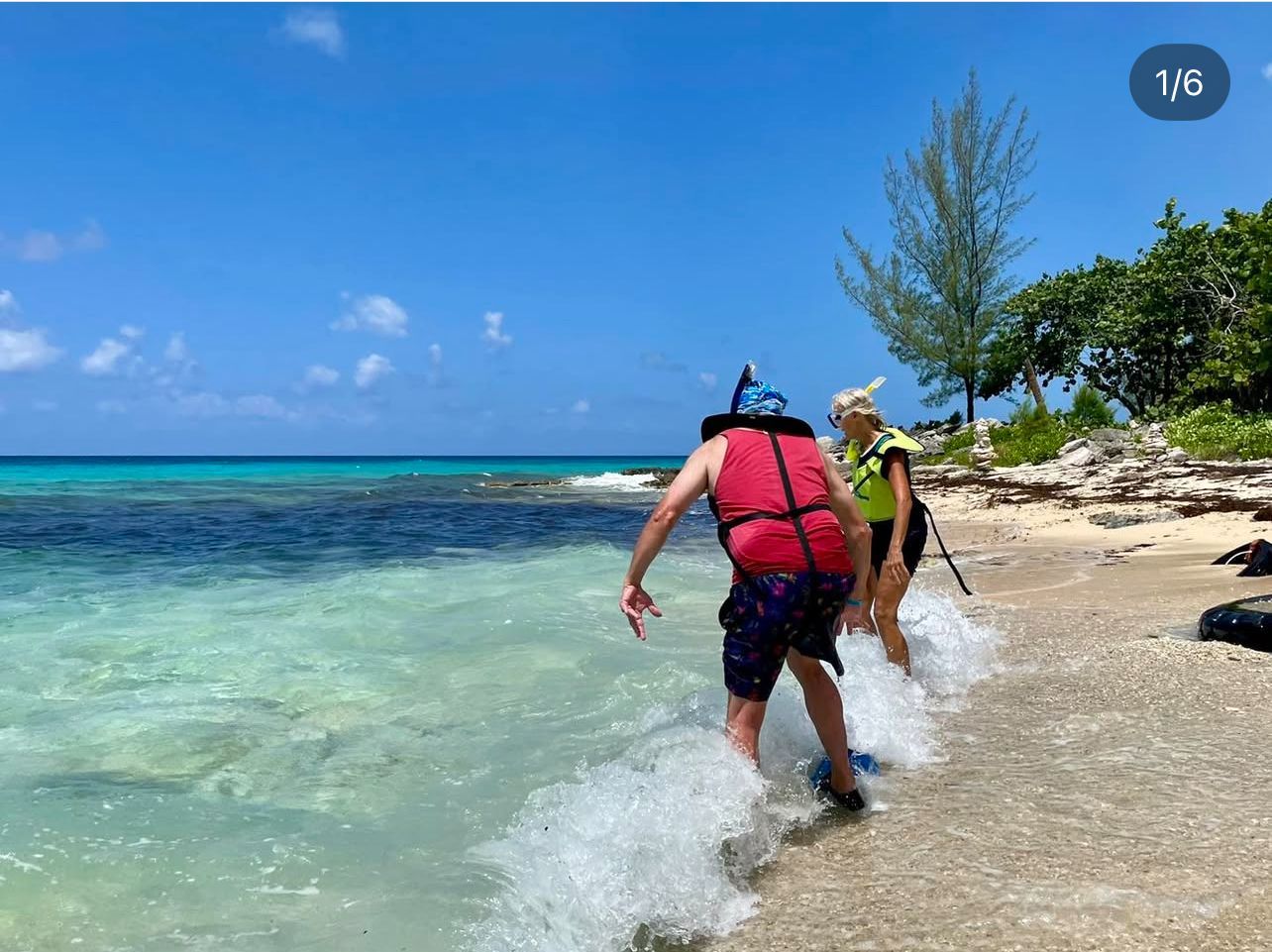 Two people in snorkeling gear walk into clear ocean water from a beach.