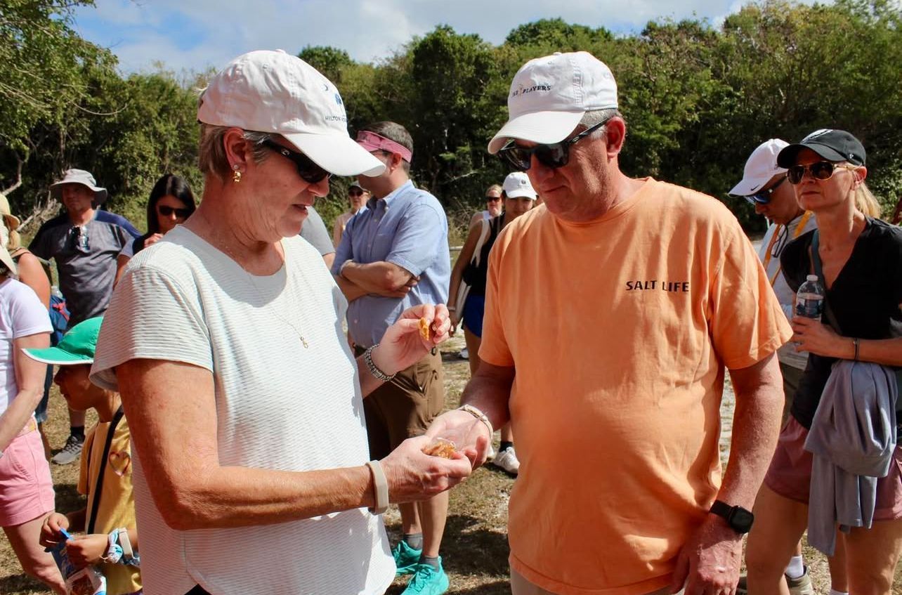 Woman shows something to a man; both wear hats outdoors, surrounded by people.