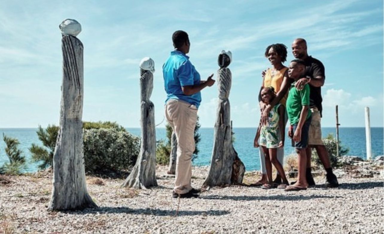 A guide explains sculptures to a family near the ocean.