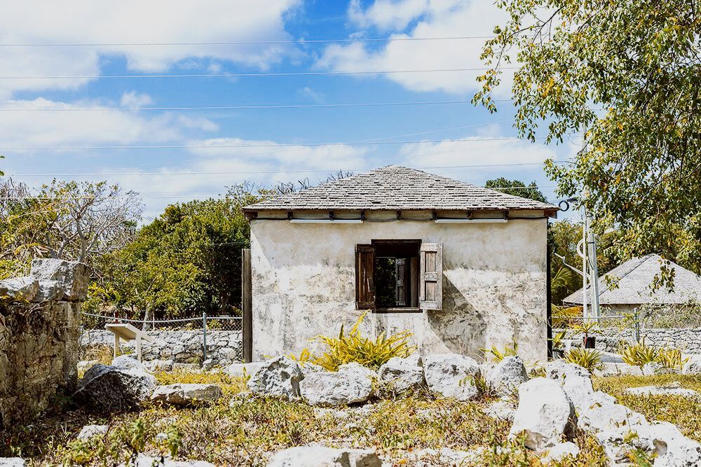 Small, weathered white building with open window in a rocky field under a blue sky.