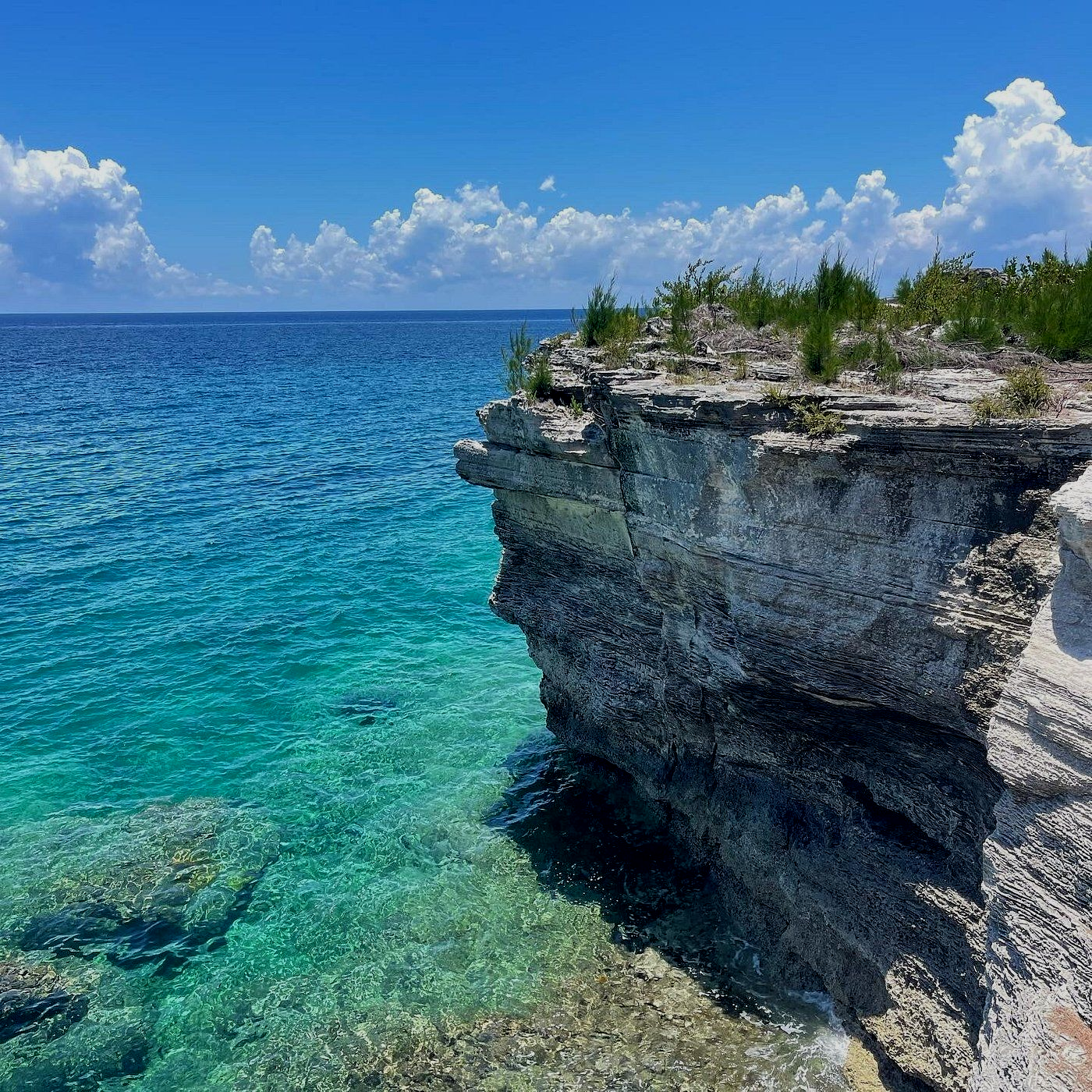 Ocean cliff with turquoise water under a blue sky with fluffy white clouds.