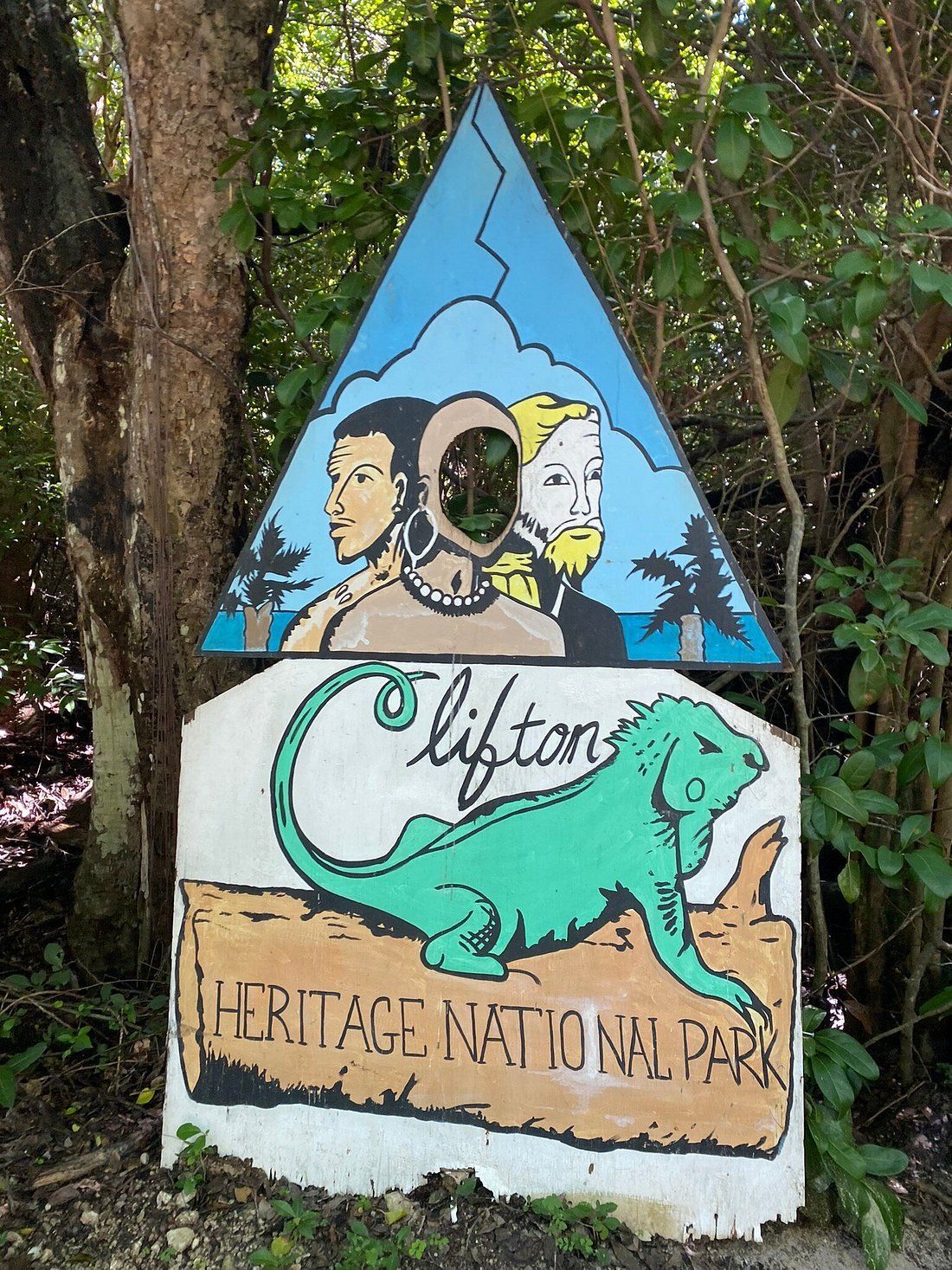 Sign for Clifton Heritage National Park: triangle with painted faces, iguana, and text on a white background.