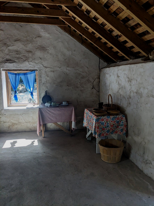 A rustic room with two tables covered in checkered and floral cloths, basket, and window with blue curtains.
