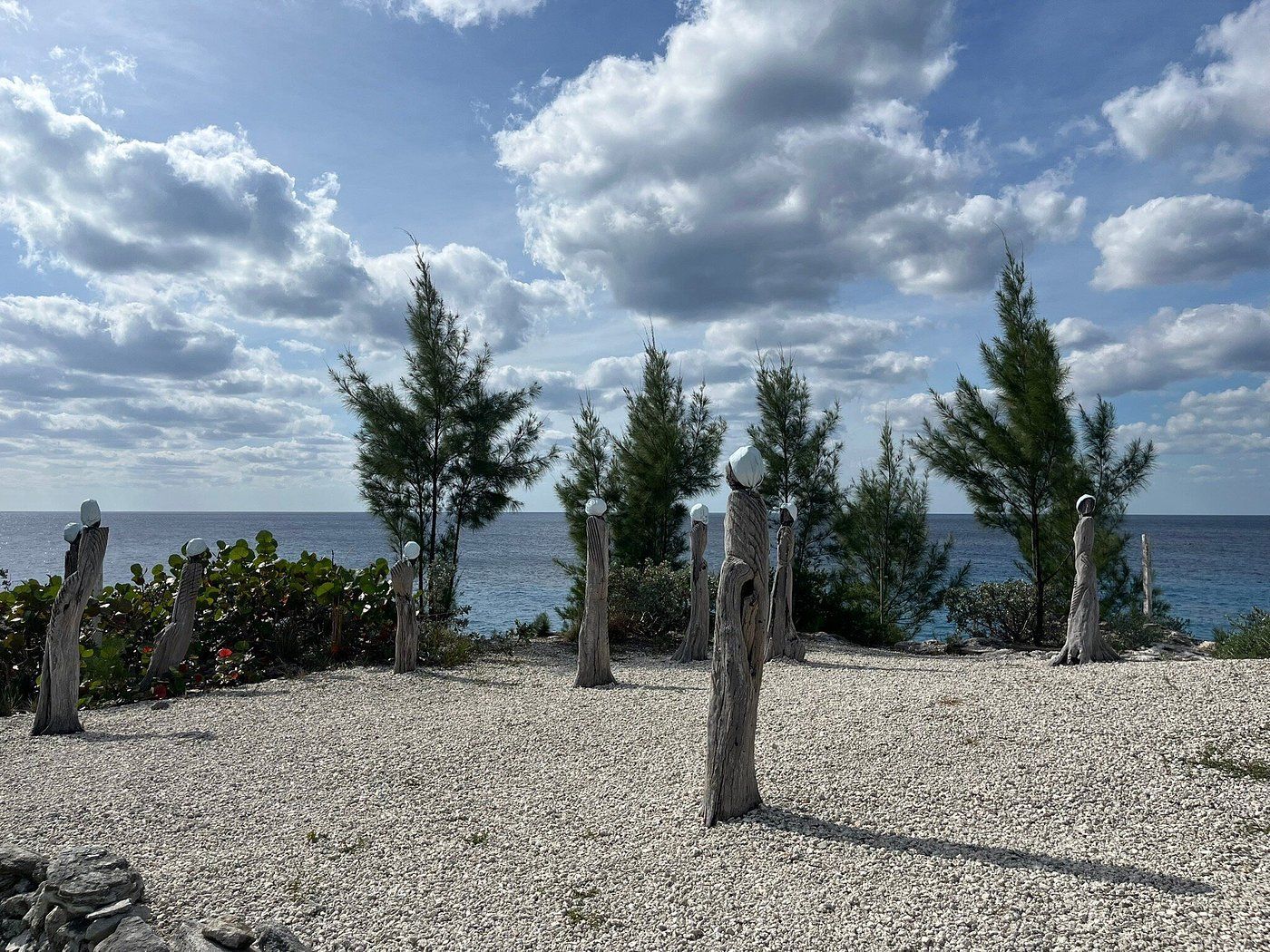 Rocky shoreline with driftwood art and trees, ocean and cloudy sky.