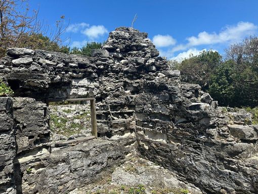 Ruins of a stone structure against a bright blue sky, surrounded by greenery.