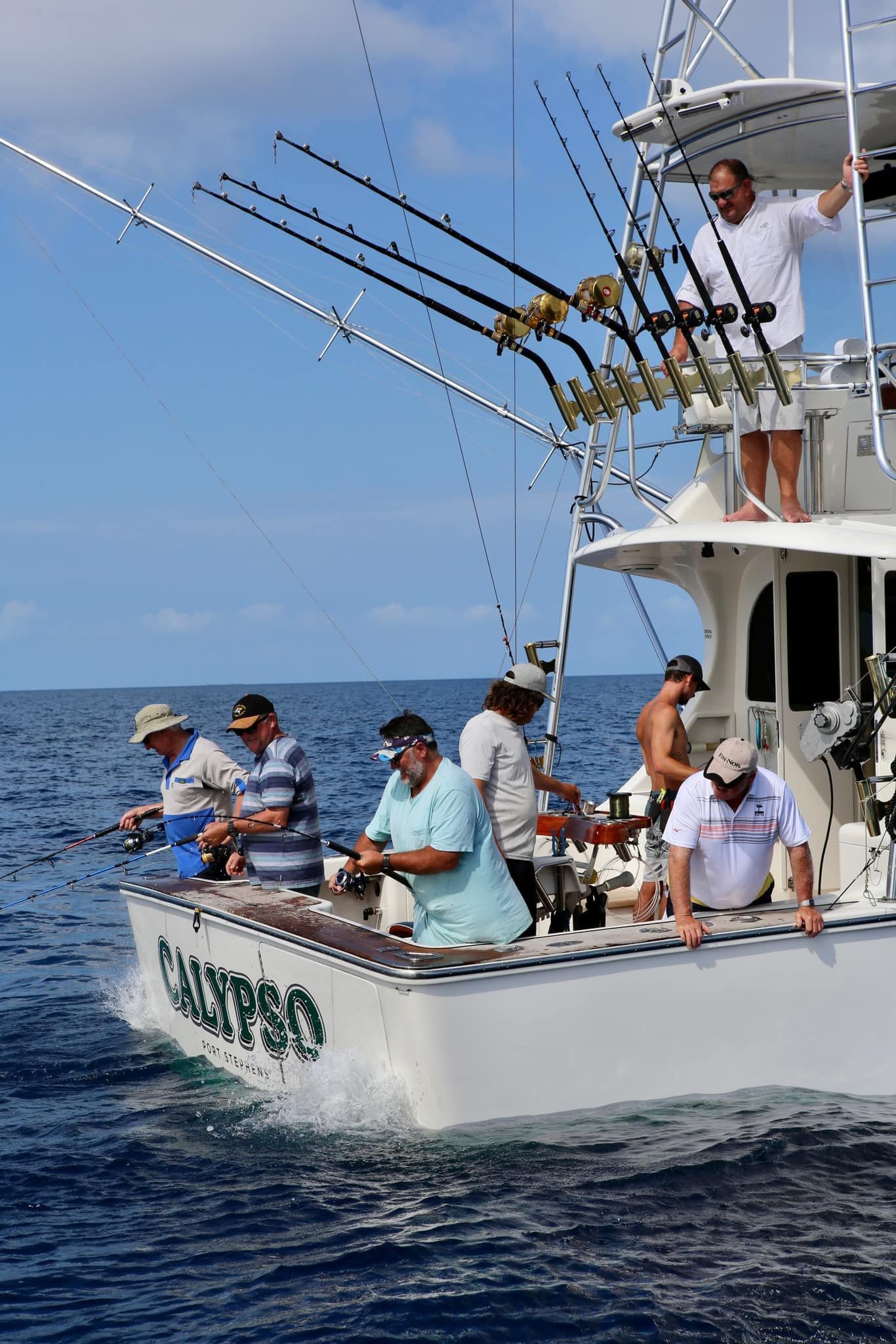 A fishing boat with several people fishing on a blue ocean on a sunny day.