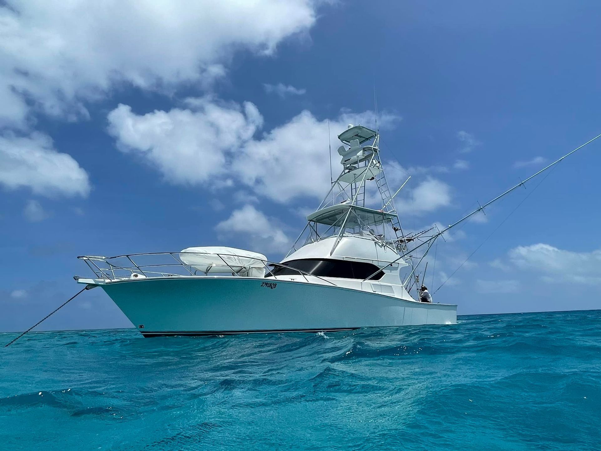 White fishing boat on turquoise water under a blue sky with fluffy clouds.