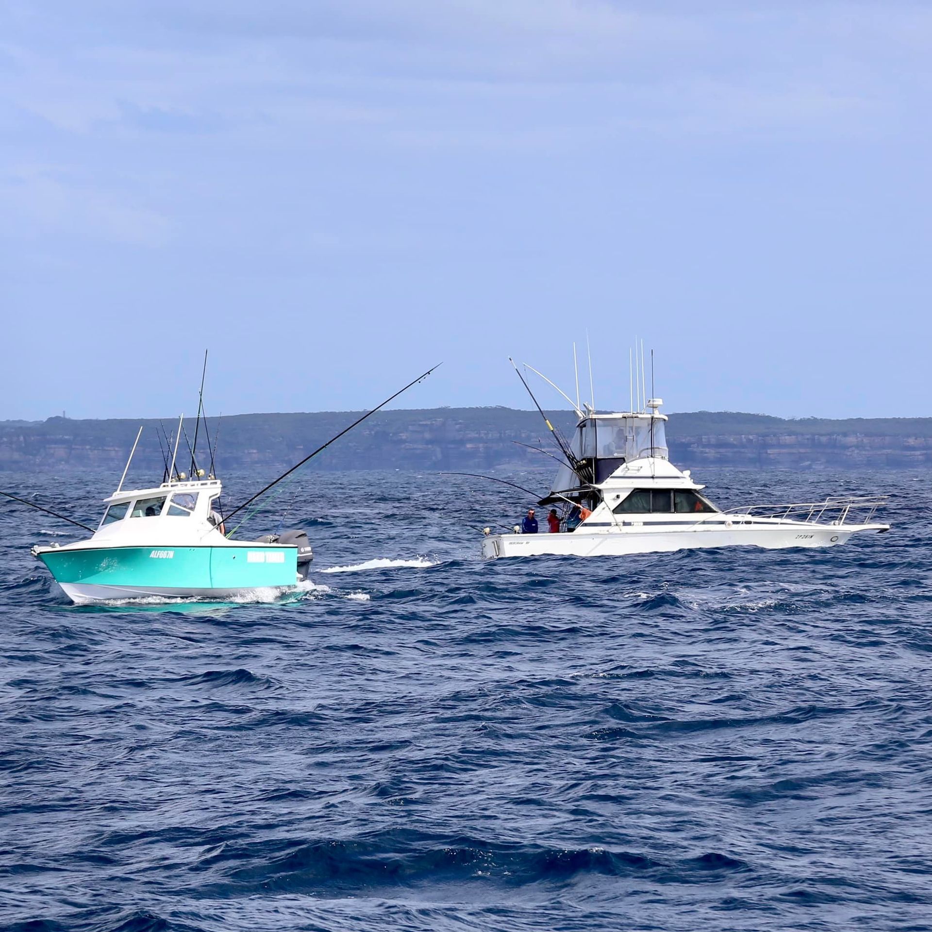 Two fishing boats on choppy blue water, one teal and one white, both with fishing rods.