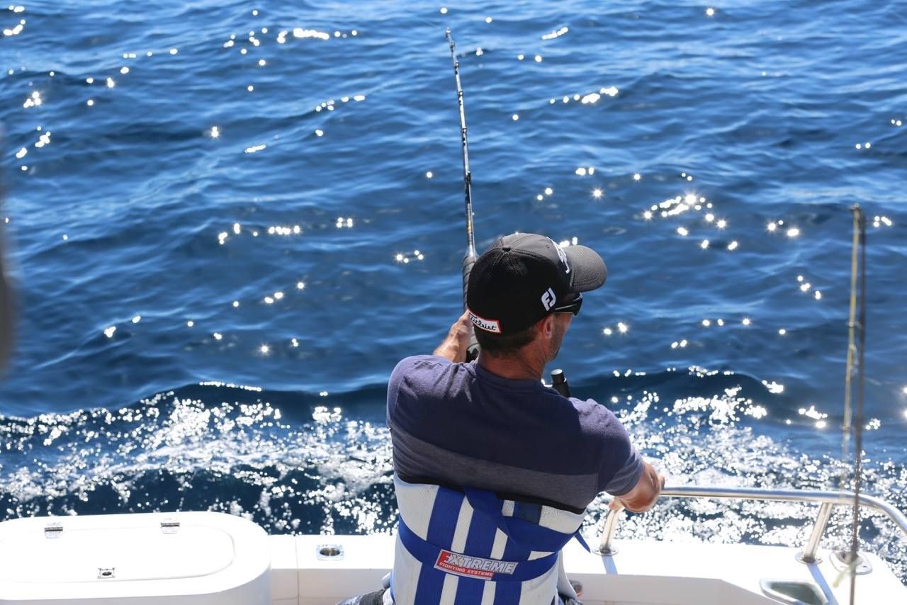 Person fishing from a boat on a sunny day; blue water and sky.