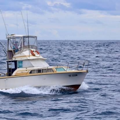 White fishing boat on the ocean, heading toward the right, with people on board.