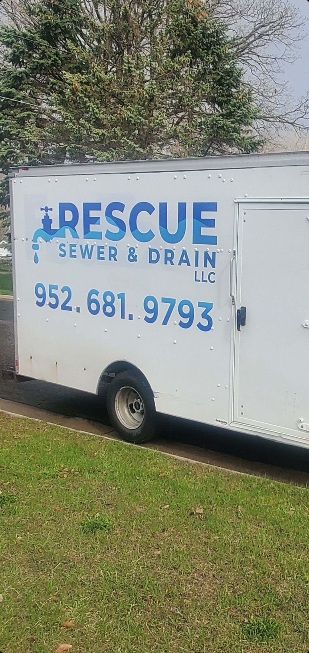A white rescue sewer and drain truck is parked in a grassy field.
