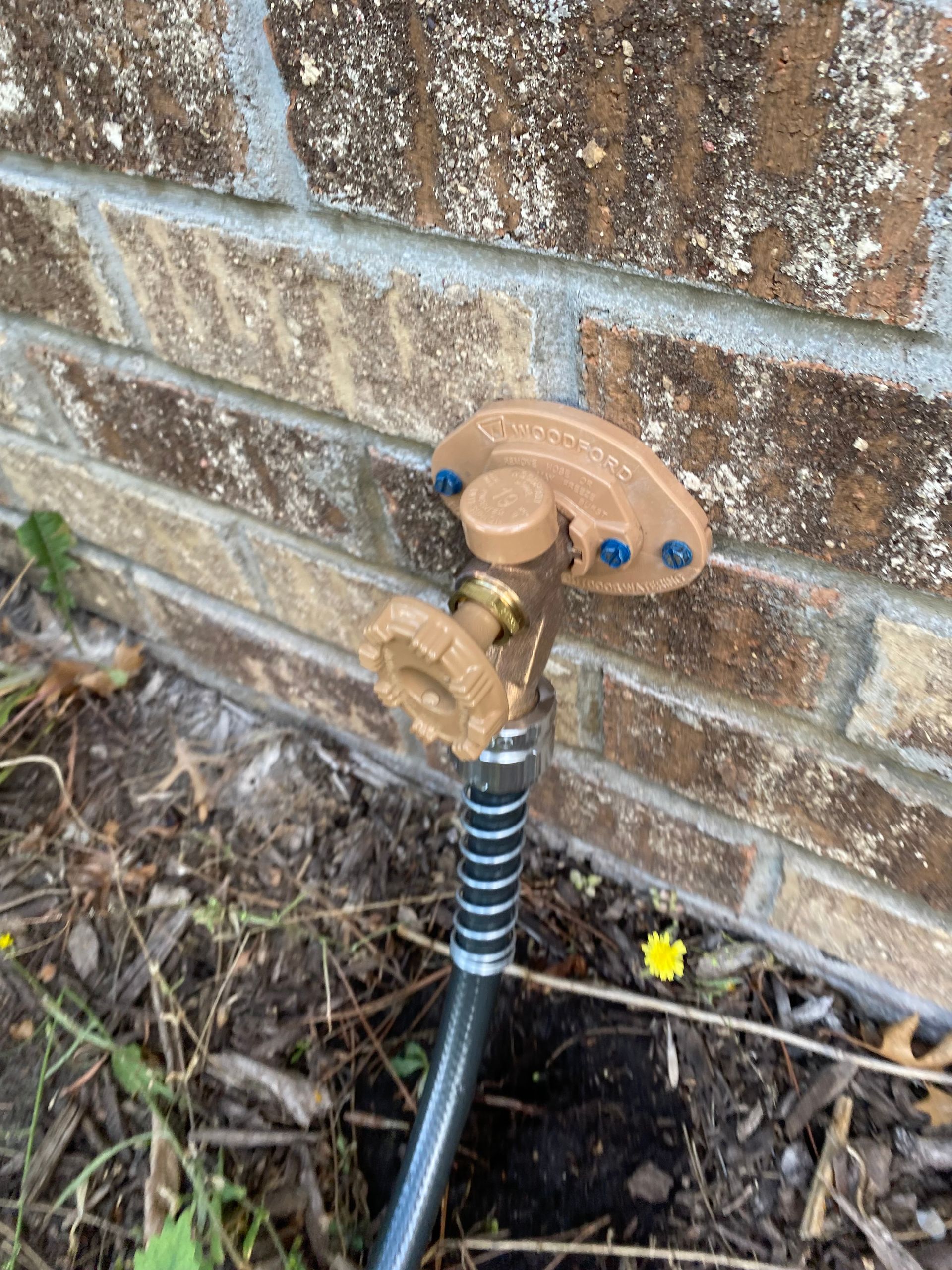 A hose with a sprinkler attached to it is sitting next to a brick wall.