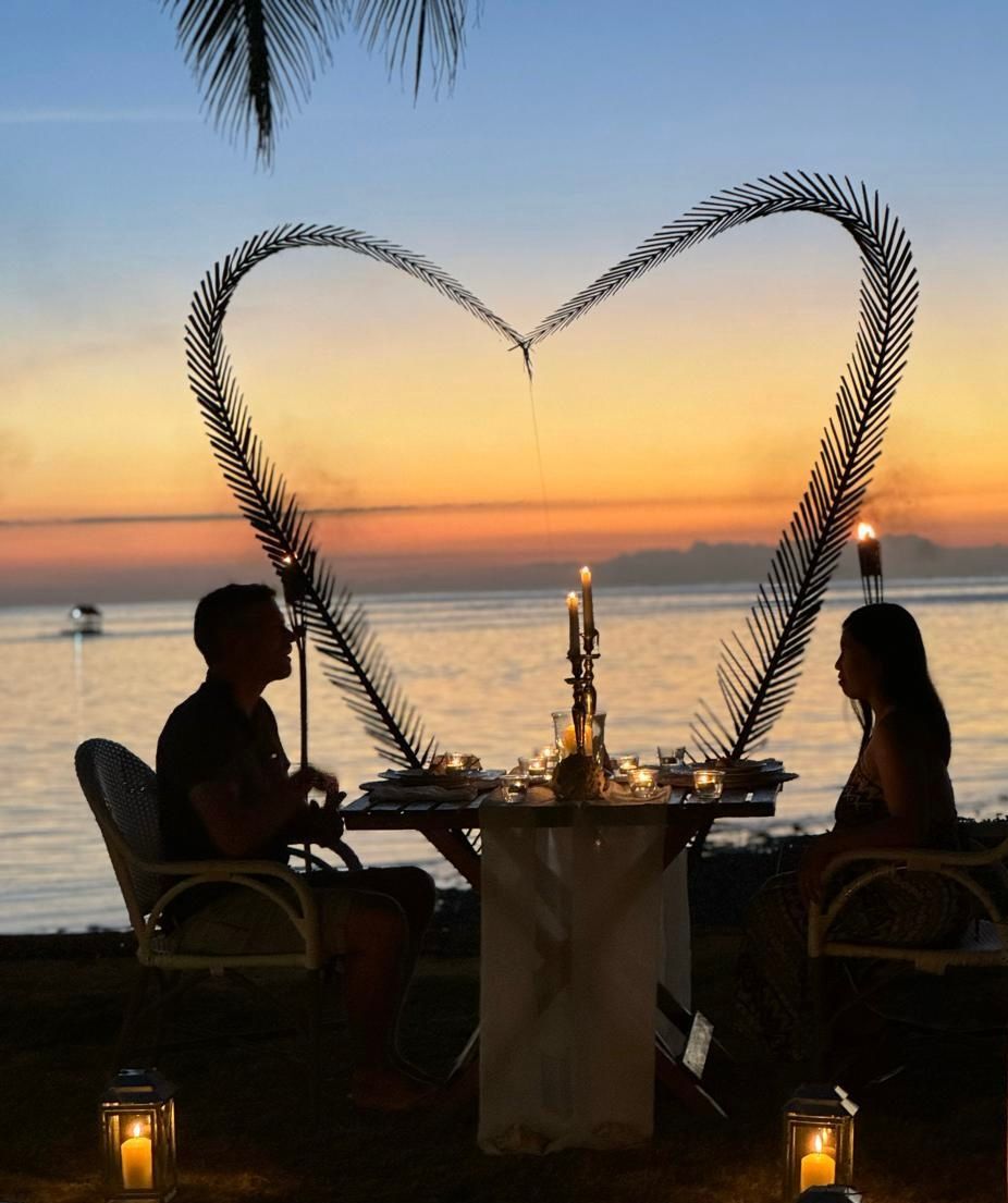 A man and woman are sitting at a table with a heart made out of palm leaves