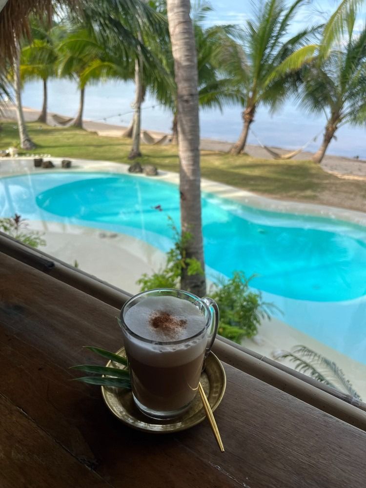A cup of coffee sits on a table in front of a pool