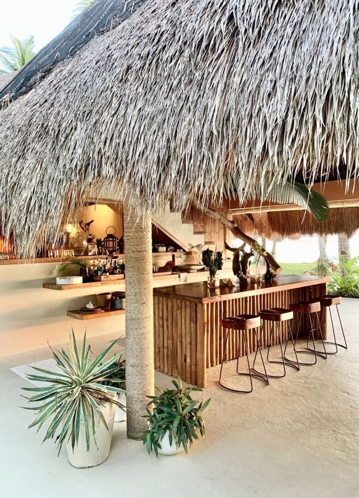 A thatched roofed restaurant with a bar and stools underneath it.