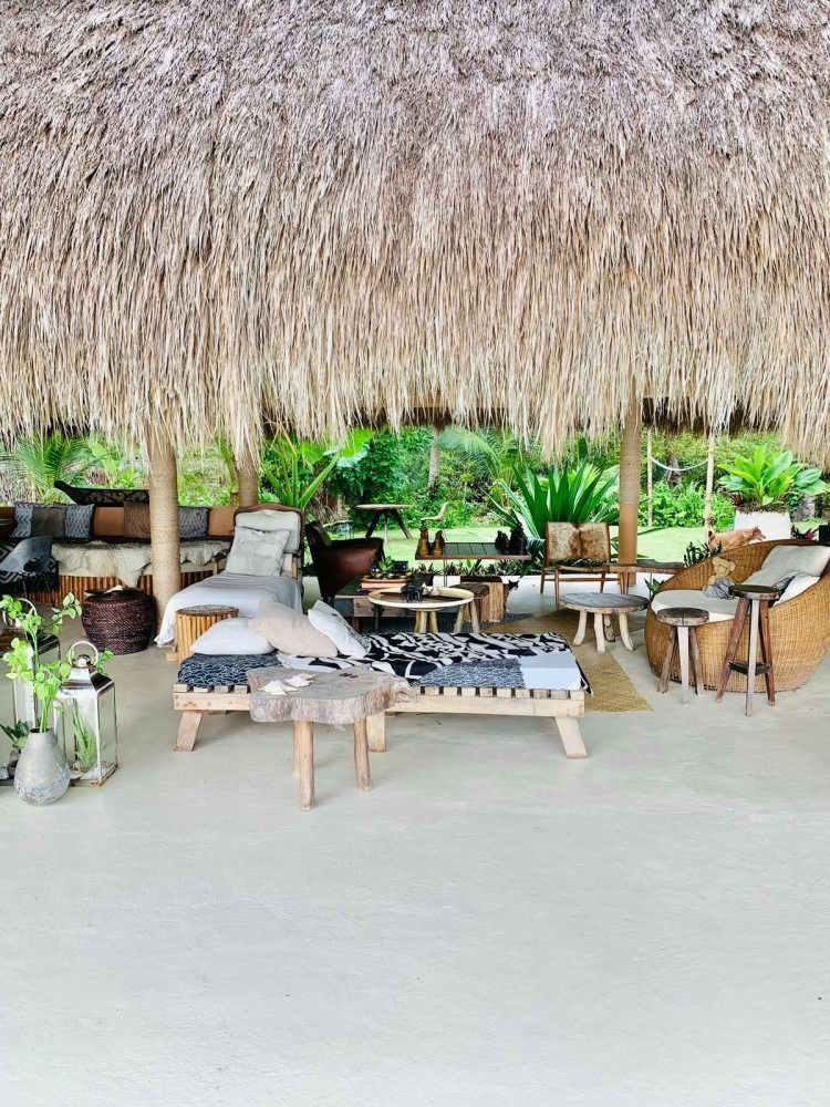 There are a lot of chairs and tables under a thatched roof.