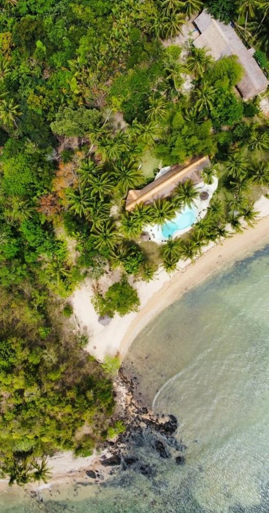 An aerial view of a tropical island with a swimming pool and a beach.