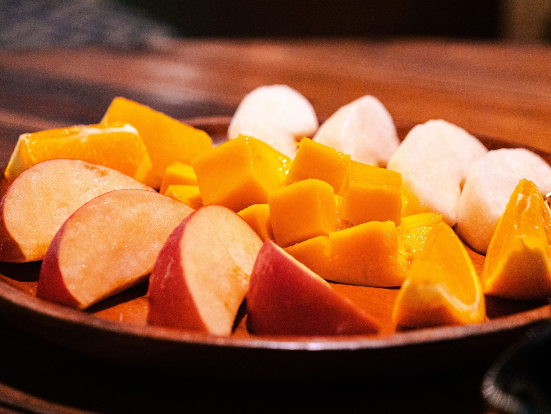 A wooden bowl filled with sliced fruit on a table.