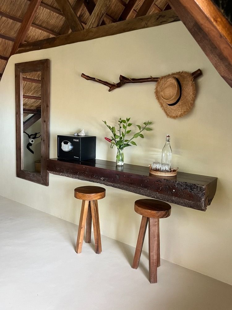A wooden table with two stools and a hat hanging on the wall.