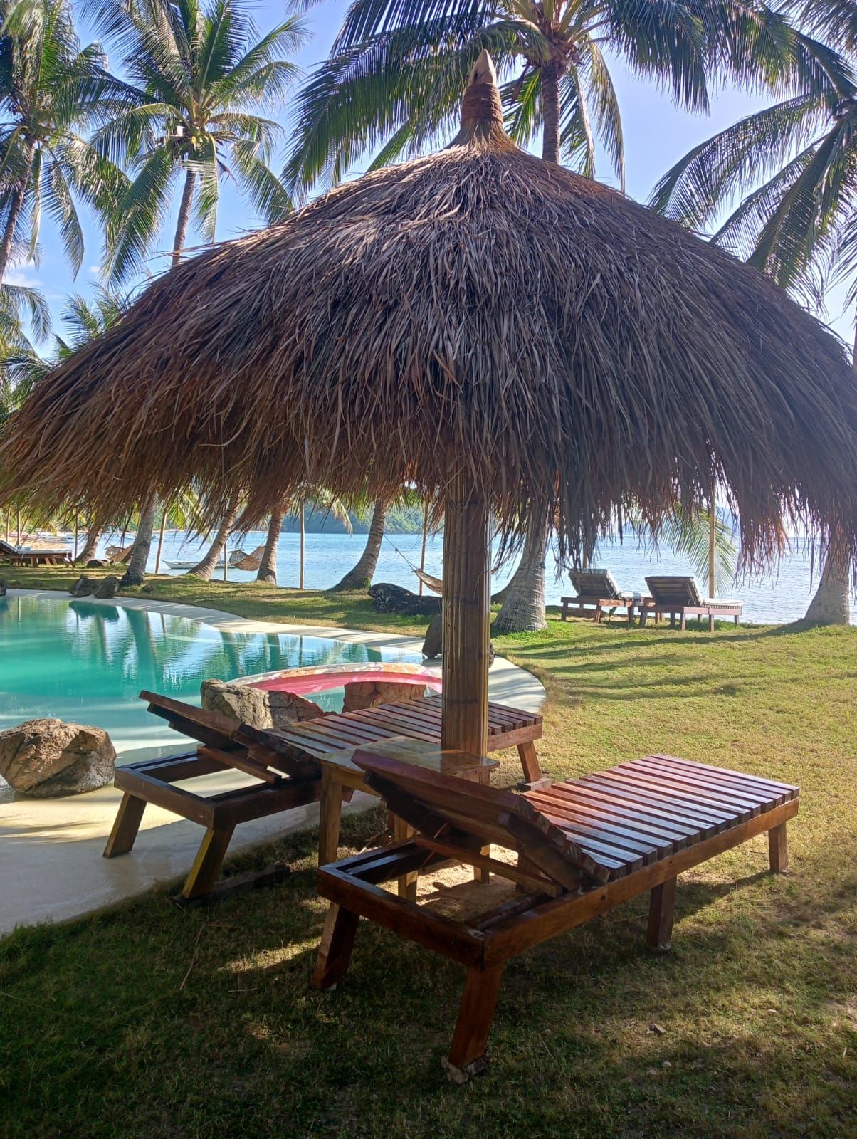 A thatched umbrella is sitting in the grass next to a swimming pool.