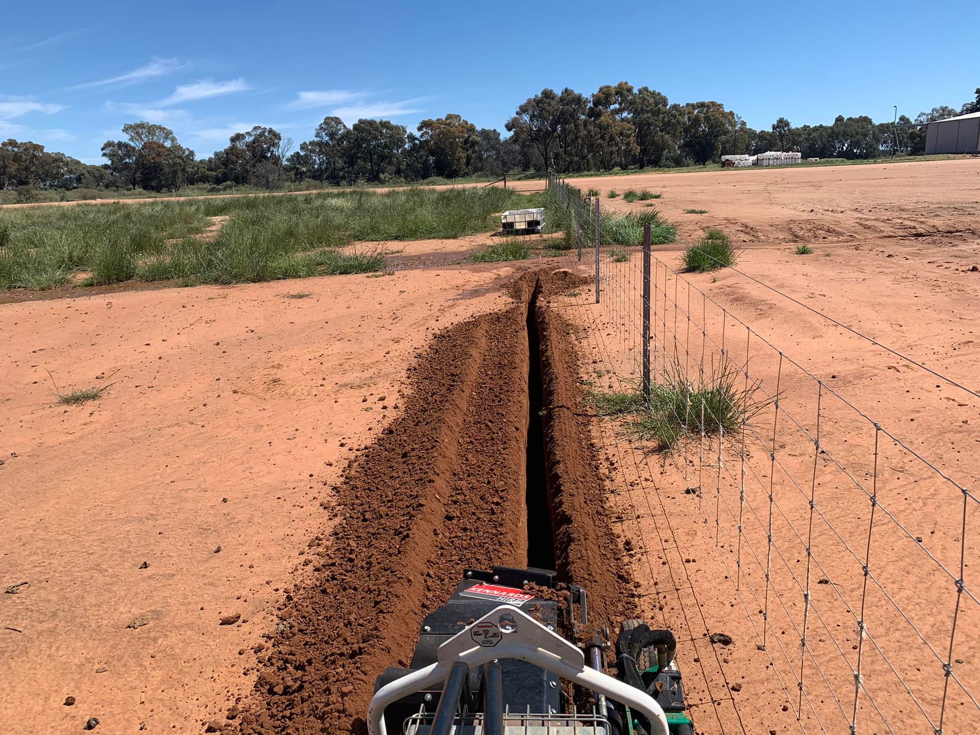 A machine is digging a trench in the dirt in a field.