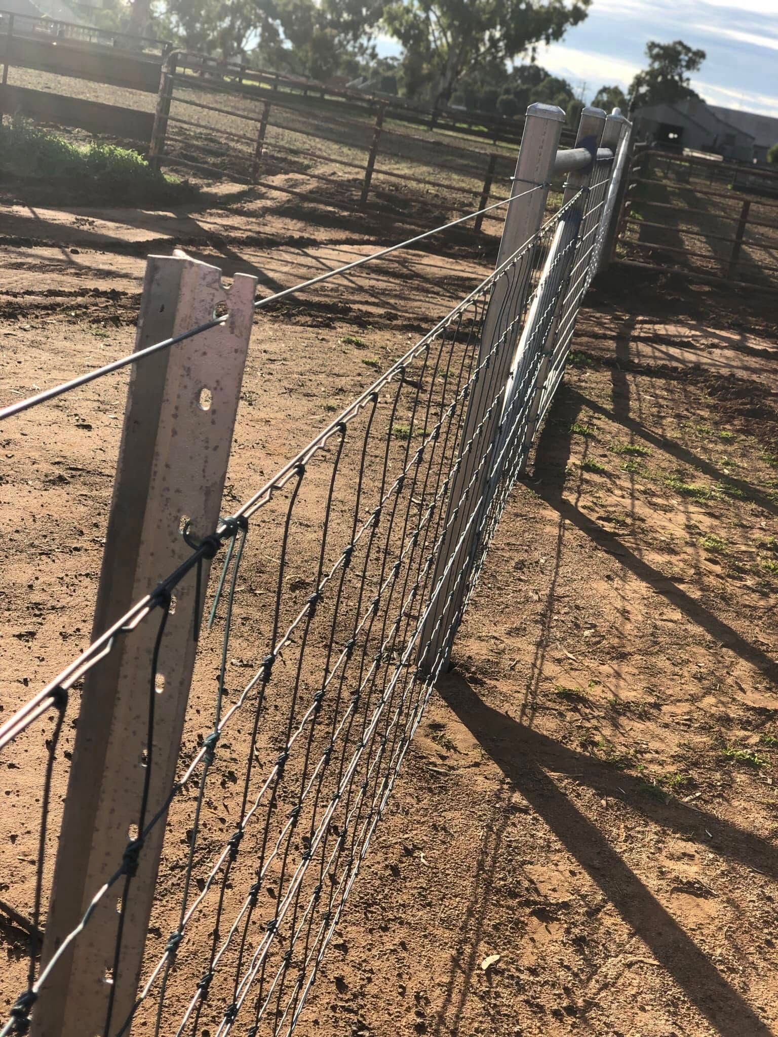 A barbed wire fence is surrounded by dirt and trees.